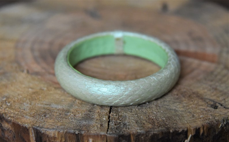 Pu&ograve; includere: Un braccialetto d'argento con un interno verde. Il braccialetto ha una superficie testurizzata.