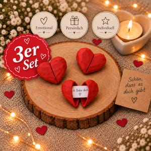 Könnte beinhalten: Drei rote geometrische herzförmige Objekte auf einer runden Holzscheibe. Ein Herz ist geöffnet und zeigt einen kleinen weißen Papierstreifen mit dem Text "Ich liebe dich". Eine quadratische Karte trägt den Text "Schön, dass es dich gibt".