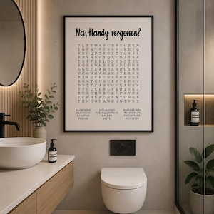 May include: A rectangular wall art print in a black frame featuring a word search puzzle on a cream background. The text at the top reads Na, Handy vergessen? followed by a grid of letters and a list of German bathroom-related vocabulary words.