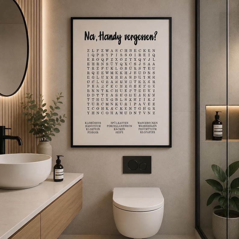 May include: A rectangular wall art print in a black frame featuring a word search puzzle on a cream background. The text at the top reads Na, Handy vergessen? followed by a grid of letters and a list of German bathroom-related vocabulary words.