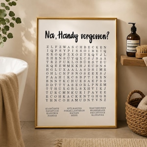 May include: A rectangular wall art print in a gold frame featuring a word search puzzle on a white background. The text at the top reads "Na, Handy vergessen?" followed by a grid of letters and a list of German words at the bottom including Klob&uuml;rste, Handtuch, Klostein, Pissoir, Sp&uuml;lkasten, Porzellanthron, Kacken, Seife, Waschbecken, Wasserhahn, Feuchttuch, and Klopapier.