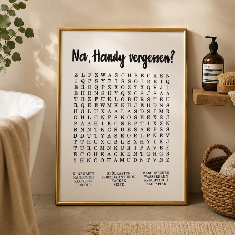 May include: A rectangular wall art print in a gold frame featuring a word search puzzle on a white background. The text at the top reads "Na, Handy vergessen?" followed by a grid of letters and a list of German words at the bottom including Klob&uuml;rste, Handtuch, Klostein, Pissoir, Sp&uuml;lkasten, Porzellanthron, Kacken, Seife, Waschbecken, Wasserhahn, Feuchttuch, and Klopapier.