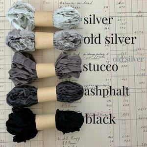 May include: Five spools of crinkled ribbon secured with tan paper bands, arranged vertically. Colors include silver, old silver, stucco, asphalt, and black. Each ribbon is labeled with its corresponding color name in black text to the right side.