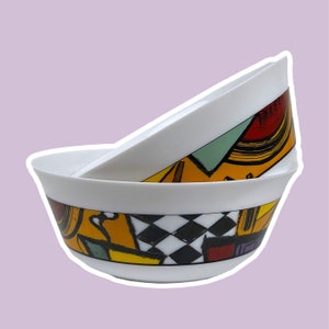 May include: Two white ceramic bowls with a geometric pattern in yellow, red, green, and black. The bowls are stacked on top of each other.
