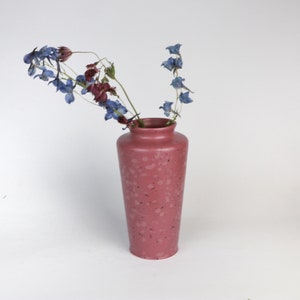Könnte beinhalten: Eine rosafarbene, gesprenkelte Keramikvase mit getrockneten blauen und violetten Blumen.