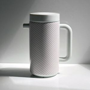 Puede incluir: Una cafetera de cerámica blanca con tapa y asa a juego. El cuerpo cilíndrico presenta un patrón de líneas diagonales rojas. La cafetera tiene un pico y está diseñada para preparar y servir café o té.