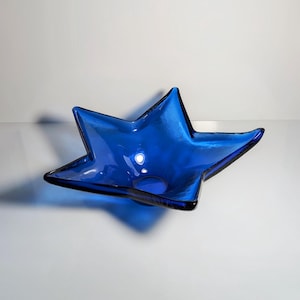 May include: A cobalt blue glass star-shaped bowl. The bowl is made of thick glass and has a slightly textured surface.