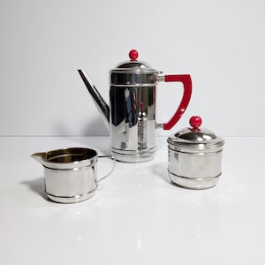 May include: A silver coffee and tea set with red accents. The set includes a teapot, creamer, and sugar bowl.