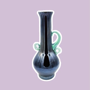 Könnte beinhalten: Eine schwarze, irisierende Glasvase mit einem bauchigen Körper und einem langen, schlanken Hals. Die Vase hat zwei grüne Glasgriffe, die sich um den Hals schlingen.