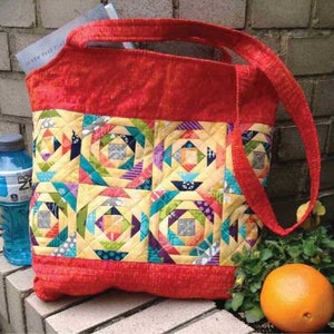 May include: A red quilted tote bag with a patchwork design featuring colorful squares and triangles. The bag has a long strap and is made of fabric.