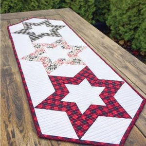 May include: A white table runner with three red, white, and black star designs. The stars are quilted and have a geometric pattern.