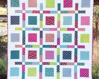 May include: A quilt pattern called "Boxed Up" with a layer cake or fat quarter friendly design. The quilt is made up of squares in various colors and patterns, including pink, blue, green, and white.