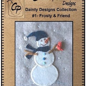 May include: Felt applique pattern for a snowman with a blue hat and scarf, holding a red cardinal. The pattern is titled "Frosty & Friend" and is part of the "Dainty Designs Collection".