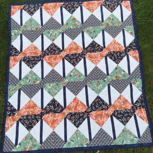 May include: A quilt with a geometric pattern of white, navy blue, green, and orange triangles. The quilt is made of fabric with floral and leaf patterns.