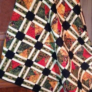 May include: A quilt with a black and white grid pattern and colorful fabric squares. The fabric squares feature a variety of floral and geometric designs in shades of red, green, brown, and yellow.