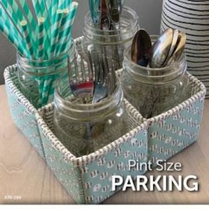 May include: A white fabric storage box with a blue and white pattern. The box has four compartments, each holding a glass jar. The jars contain silverware and straws. The box has the text "Pint Size Parking" printed on the front.