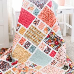 May include: A colorful patchwork quilt with a geometric design, featuring squares and rectangles in various floral and patterned fabrics. The quilt is draped over a chair, with the word "Craftsman" in a banner at the top and "Amy Smart Diary of a Quilter" at the bottom.
