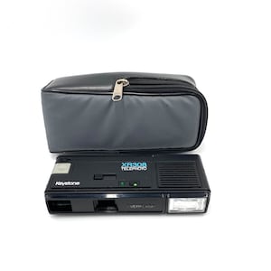 May include: A black Keystone XR308 Telephoto camera with a built-in flash and a gray carrying case.