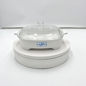 May include: White ceramic square baking dish with a glass lid. The dish has a blue and white logo with a wavy line design.