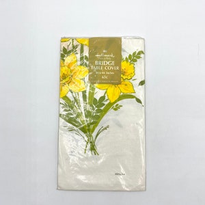 May include: A white plastic-wrapped package containing a yellow and green floral print bridge table cover. The package has the text "Hallmark Home & Party Bridge Table Cover 34 x 44 inches 65c" printed on it.