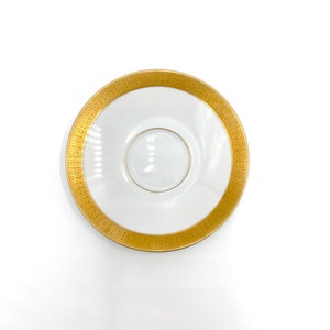 Puede incluir: Un platillo blanco con un borde dorado y un círculo central dorado. El platillo es perfecto para servir té o café.