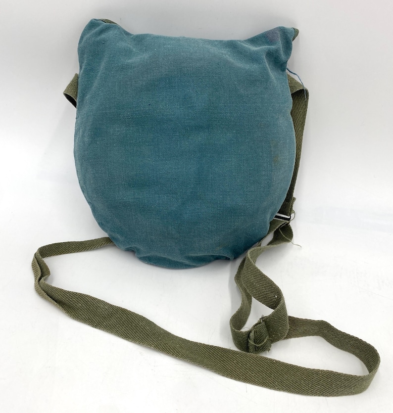Op de afbeelding: Een teal-kleurige, afgeronde tas met een groene riem. De tas heeft een getextureerde uitstraling en een flap aan de bovenkant. De riem is verstelbaar en gemaakt van duurzaam, geweven materiaal. De tas is ontworpen om over de schouder te worden gedragen.