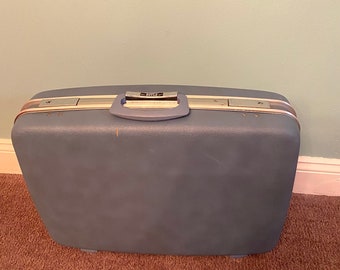 May include: A blue hard-sided suitcase with a silver handle and a silver latch. The suitcase has a slightly worn look.