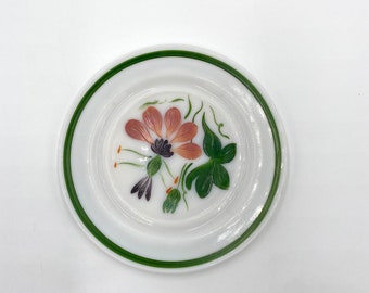May include: A white ceramic plate with a green rim and a hand-painted floral design. The flower is pink with a purple center and green leaves.