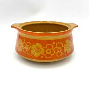 Könnte beinhalten: Eine braune Keramik-Auflaufform mit einem breiten orangefarbenen Band und einem floralen Muster in einem helleren Braunton.