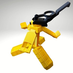 以下が含まれることがあります： 黒い調節可能なアームが付いた黄色のプラスチック製の携帯電話スタンド。スタンドは円形のベースと、折り畳み式の3本の脚を持っています。アームは、携帯電話をさまざまな角度で保持するように調整できます。