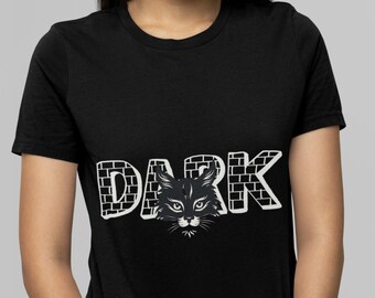 Puede incluir: Camiseta negra con un gráfico blanco de la palabra "DARK" con la cara de un gato negro asomándose desde el medio de la palabra.