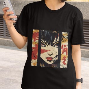 Pode incluir: Camiseta preta com uma estampa gráfica de um rosto de mulher com detalhes em vermelho e amarelo. O gráfico inclui texto japonês.
