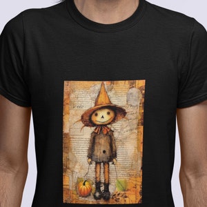 以下が含まれることがあります： ヴィンテージスタイルのイラストが描かれた黒いTシャツ。イラストには、小さなカボチャを持ったカカシが描かれています。カカシは茶色の帽子と茶色のジャケットを着ています。背景は、色あせたヴィンテージ風のテクスチャのある紙です。