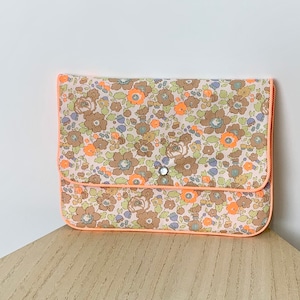 Puede incluir: Una pequeña bolsa de estampado floral con un borde de color melocotón y un cierre de botón único.