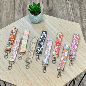 May include: Eight colourful keychains with floral patterns and silver key rings. The keychains are made of fabric and have a variety of floral designs.