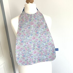 May include: A light blue bib with a floral pattern in pink, green, and blue. The bib has a blue trim and a blue strap.