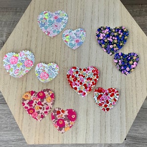 以下が含まれることがあります： ピンク、赤、青、白の様々な花柄の布製のハート形が9つ。ハートは薄い茶色の木製の表面に並べられています。