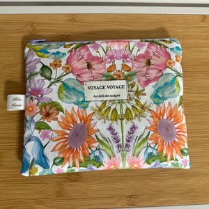 May include: A floral print pouch with a zipper closure. The pouch features a vibrant pattern of pink poppies, orange sunflowers, and other colorful flowers on a white background. The text "VOYAGE VOYAGE" is printed on a label.