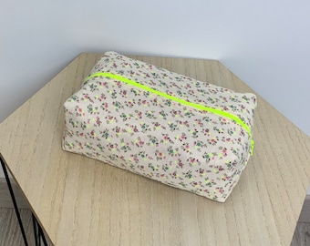 May include: A small, rectangular zippered pouch with a floral print and a bright yellow zipper. The pouch is made of a soft, light-colored fabric.