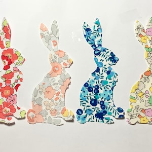 May include: Four fabric bunny silhouettes in different floral patterns. The bunnies are in shades of pink, blue, yellow, and red.