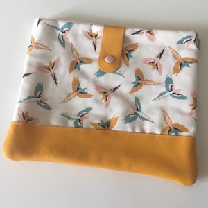 May include: A white fabric tablet case with a yellow leather bottom and a pink button closure. The fabric features a pattern of colorful birds.