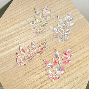 Peut inclure: Quatre feuilles en papier à motifs floraux, découpées en forme de branche, sur une surface en bois brun clair.