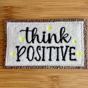 Embroidered "Think Positive" label to personalize your clothing, accessories, or creations; bronze glitter faux leather backing
