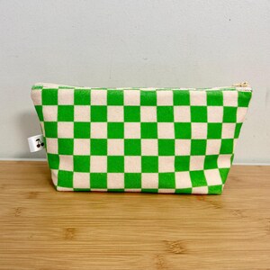 Può includere: Una trousse da trucco a quadri verdi e bianchi con chiusura a zip.