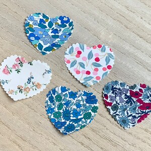 Può includere: Cinque toppe di tessuto a forma di cuore con diversi motivi floreali. Le toppe sono in tonalità di blu, rosa e bianco.