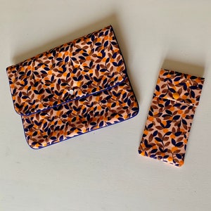 Peut inclure: Deux pochettes en tissu avec un motif floral dans les tons orange, marron et bleu. La plus grande pochette a un rabat rabattable et une bordure bleue. La plus petite pochette est rectangulaire.