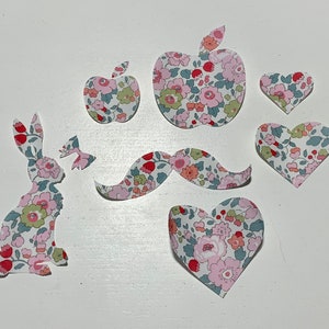 May include: A set of fabric cutouts in a floral pattern, including a rabbit, two apples, a mustache, and three hearts.