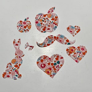 May include: A set of fabric appliques featuring a bunny, a mustache, two hearts, and two apples. The appliques are all in a floral pattern with pink, red, and white colors.