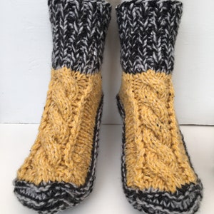 May include: A pair of knitted socks with a black and white pattern on the top and a yellow cable knit pattern on the bottom.