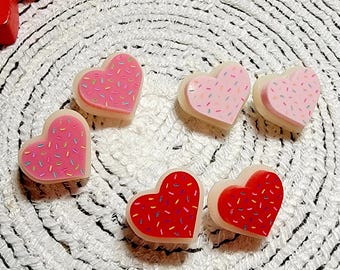 May include: Five heart-shaped resin ornaments with colorful sprinkles. The hearts are in two colors: pink and red.
